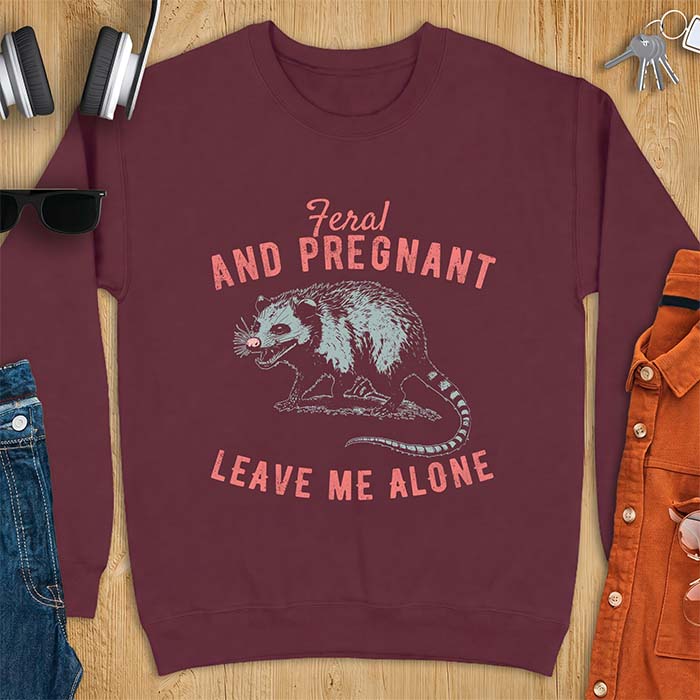 Maroon sweatshirt with a graphic of a hissing opossum baring its teeth with a striped tail, plus the text Feral And Pregnant Leave Me Alone.