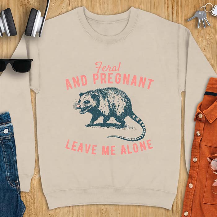 Sand sweatshirt with a graphic of a hissing opossum baring its teeth with a striped tail, plus the text Feral And Pregnant Leave Me Alone.