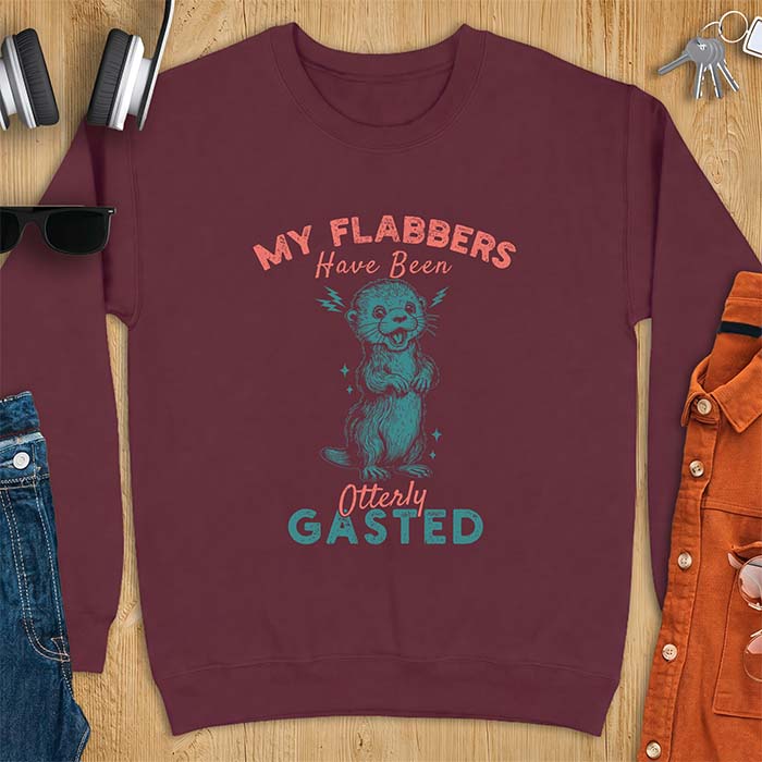 Maroon sweatshirt with a graphic of a startled otter standing upright with paws clasped and mouth open in shock with lightning bolts on either side, featuring the text My Flabbers Have Been Otterly Gasted.