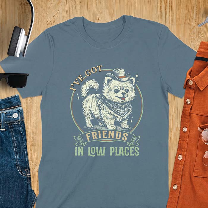 Indigo Blue t-shirt with a vintage western illustration of a fluffy Pomeranian wearing a cowboy hat and a paisley bandana, with the text I've Got arched above it and Friends In Low Places below it