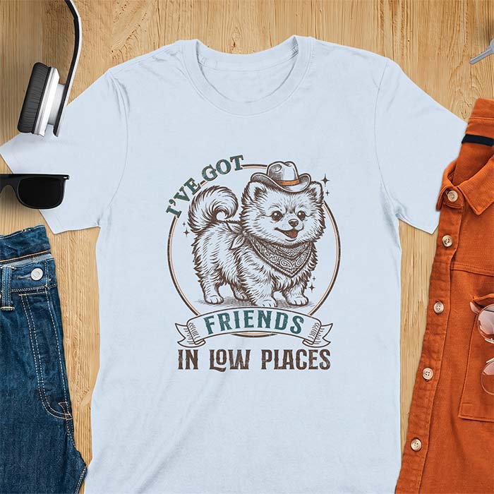 Light Blue t-shirt with a vintage western illustration of a fluffy Pomeranian wearing a cowboy hat and a paisley bandana, with the text I've Got arched above it and Friends In Low Places below it