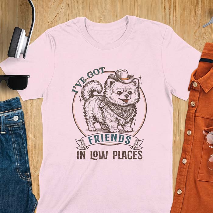 Light Pink t-shirt with a vintage western illustration of a fluffy Pomeranian wearing a cowboy hat and a paisley bandana, with the text I've Got arched above it and Friends In Low Places below it