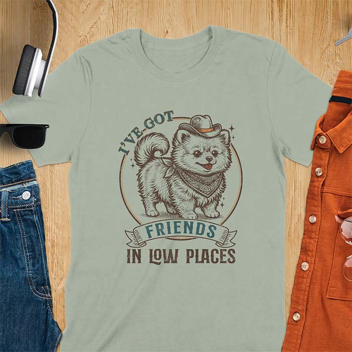 Sage t-shirt with a vintage western illustration of a fluffy Pomeranian wearing a cowboy hat and a paisley bandana, with the text I've Got arched above it and Friends In Low Places below it
