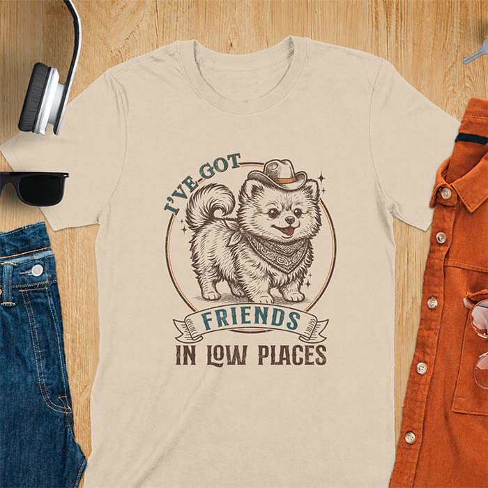 Sand t-shirt with a vintage western illustration of a fluffy Pomeranian wearing a cowboy hat and a paisley bandana, with the text I've Got arched above it and Friends In Low Places below it