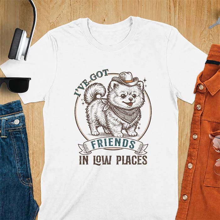 White t-shirt with a vintage western illustration of a fluffy Pomeranian wearing a cowboy hat and a paisley bandana, with the text I've Got arched above it and Friends In Low Places below it