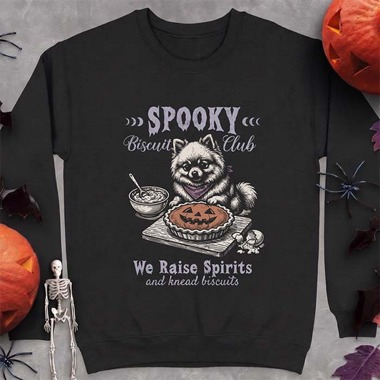 Black sweatshirt with a Halloween graphic of a Pomeranian wearing a plaid bandana sitting behind a jack-o'-lantern pumpkin pie on a cutting board with a mixing bowl, spoon and a cracked egg nearby and the text Spooky Biscuit Club, We Raise Spirits and knead biscuits