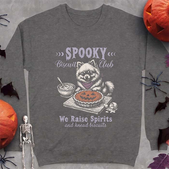 Dark Heather sweatshirt with a Halloween graphic of a Pomeranian wearing a plaid bandana sitting behind a jack-o'-lantern pumpkin pie on a cutting board with a mixing bowl, spoon and a cracked egg nearby and the text Spooky Biscuit Club, We Raise Spirits and knead biscuits