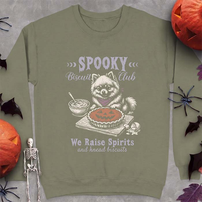 Military Green sweatshirt with a Halloween graphic of a Pomeranian wearing a plaid bandana sitting behind a jack-o'-lantern pumpkin pie on a cutting board with a mixing bowl, spoon and a cracked egg nearby and the text Spooky Biscuit Club, We Raise Spirits and knead biscuits