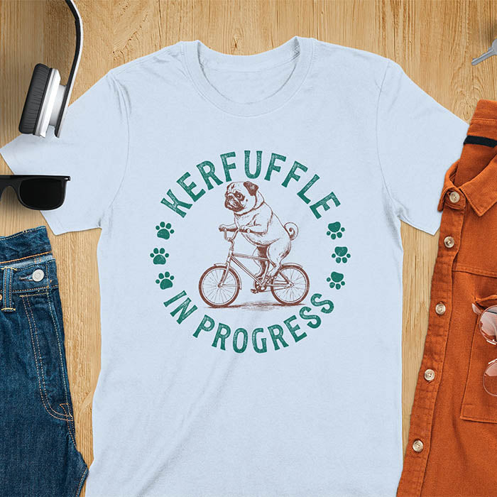 Pug on bicycle sketch-style graphic with Kerfuffle In Progress text and paw prints on light blue t-shirt