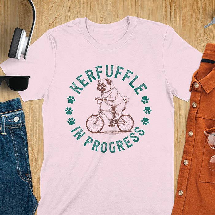 Pug on bicycle sketch-style graphic with Kerfuffle In Progress text and paw prints on light pink t-shirt