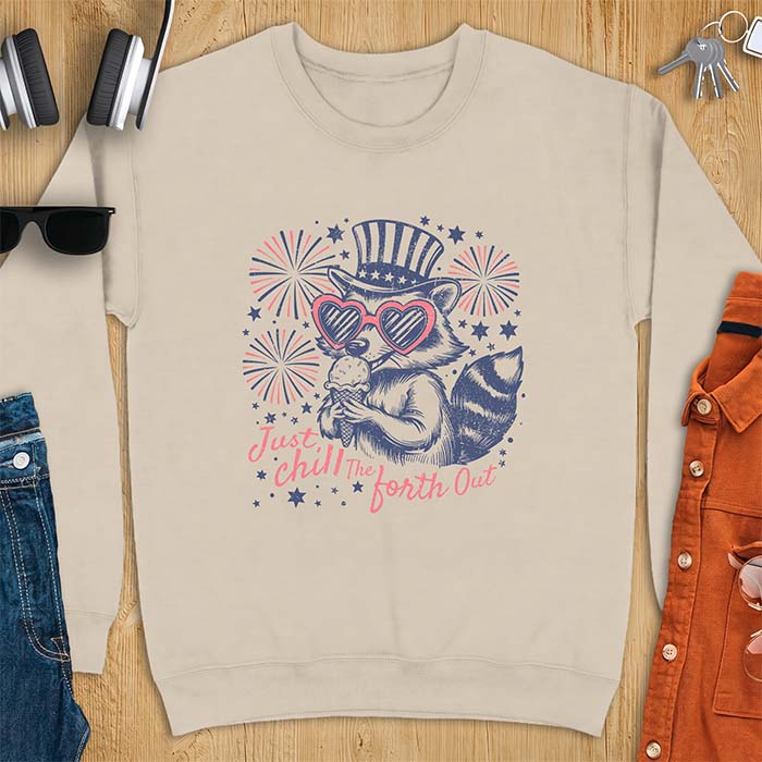 Sand sweatshirt with a graphic of a raccoon in a striped top hat and heart-shaped sunglasses eating an ice cream cone in front of fireworks and stars, printed with the text Just Chill The Forth Out