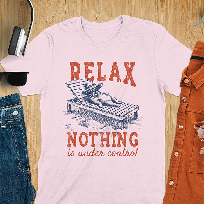 Light pink t-shirt featuring a bulldog wearing a straw hat lounging on a beach chair with text Relax Nothing Is Under Control in vintage red lettering