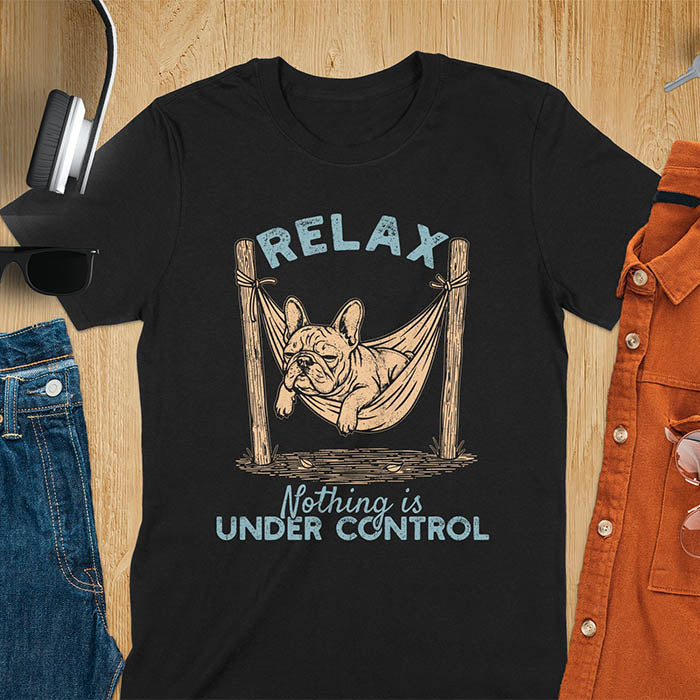 Black t-shirt with vintage-inspired illustration. Retro graphic features French bulldog relaxing in hammock with 'Relax' and 'Nothing is Under Control' text in distressed typography. Quirky zen humor meme design.