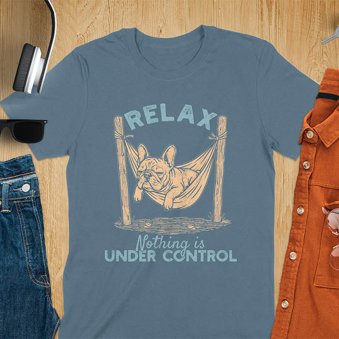 Indigo blue t-shirt with vintage-inspired illustration. Retro graphic features French bulldog relaxing in hammock with 'Relax' and 'Nothing is Under Control' text in distressed typography. Quirky zen humor meme design.