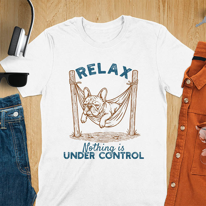 White t-shirt with vintage-inspired illustration. Retro graphic features French bulldog relaxing in hammock with 'Relax' and 'Nothing is Under Control' text in distressed typography. Quirky zen humor meme design.