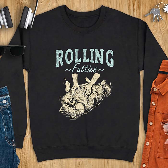 Black sweatshirt with a graphic of a fluffy Pomeranian rolled onto its back getting a belly rub from two hands and the text Rolling Fatties