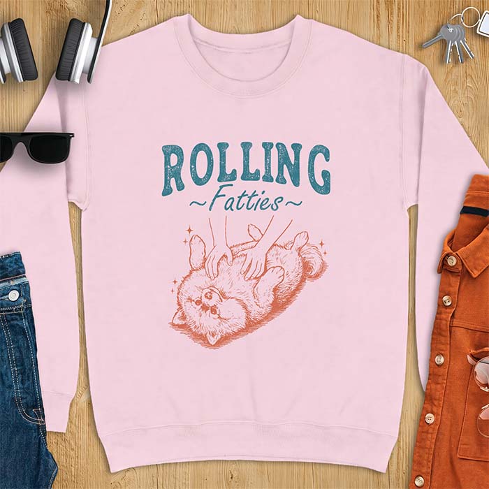 Light Pink sweatshirt with a graphic of a fluffy Pomeranian rolled onto its back getting a belly rub from two hands and the text Rolling Fatties