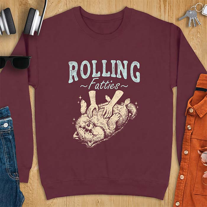 Maroon sweatshirt with a graphic of a fluffy Pomeranian rolled onto its back getting a belly rub from two hands and the text Rolling Fatties