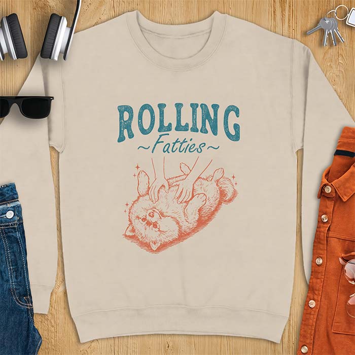 Sand sweatshirt with a graphic of a fluffy Pomeranian rolled onto its back getting a belly rub from two hands and the text Rolling Fatties