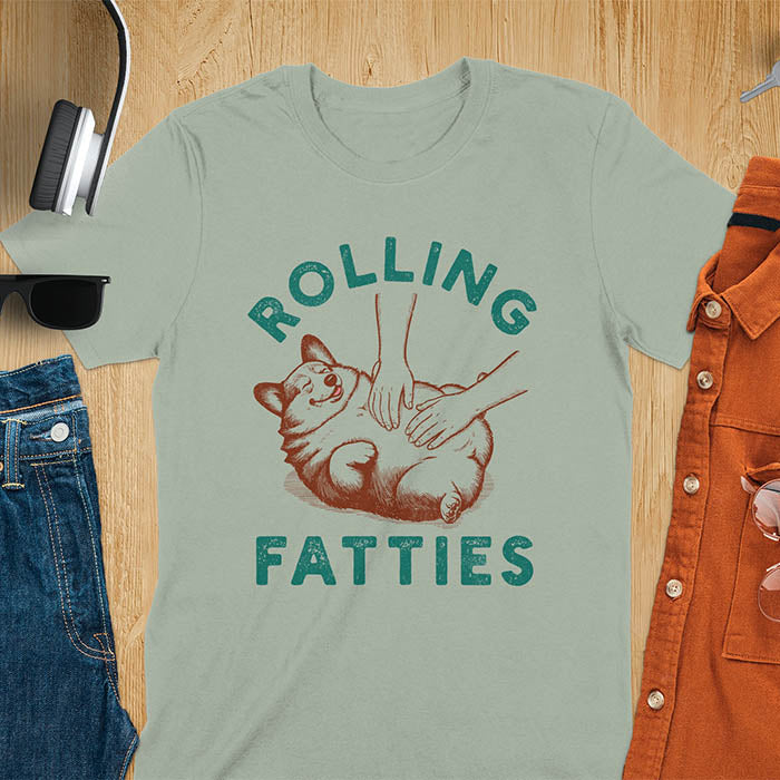 Chubby corgi illustration enjoying tummy rubs with Rolling Fatties text in textured lettering on sage green tee