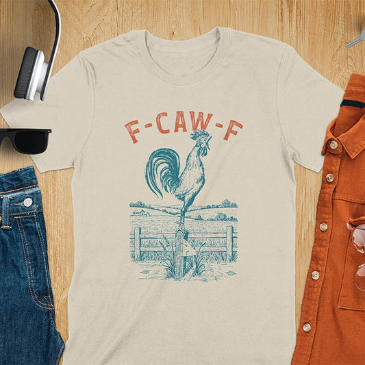 Sand color t-shirt with F-CAW-F text and detailed rooster illustration standing on wooden fence in vintage farm scene style