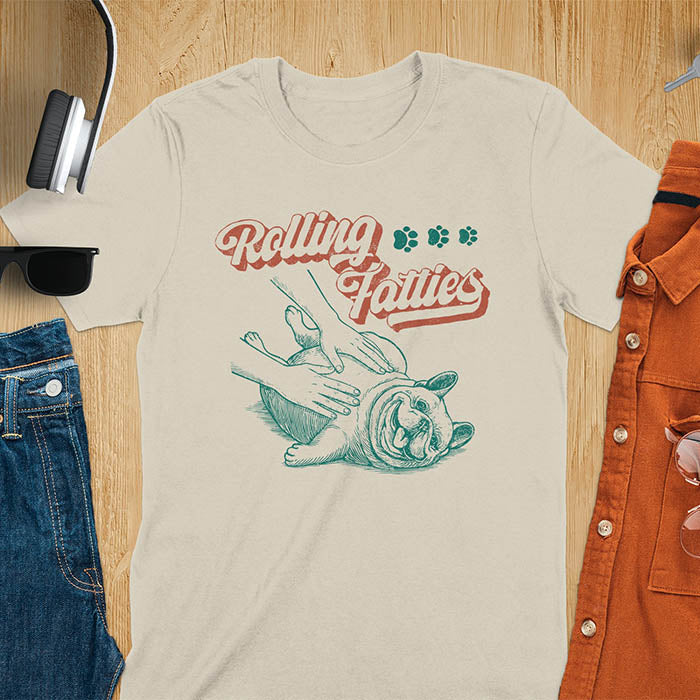 Sand color t-shirt with Rolling Fatties script text and French Bulldog being petted by human hands in line drawing style.