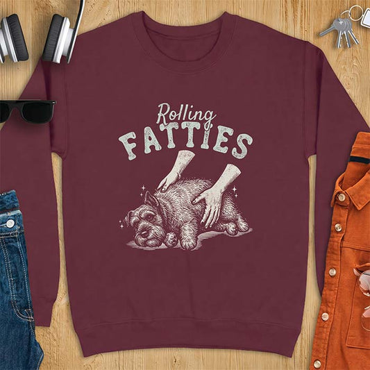 Maroon sweatshirt with a graphic of a scruffy Schnauzer lying curled on the ground while two hands reach in to scratch and pet it, plus the text Rolling Fatties above.