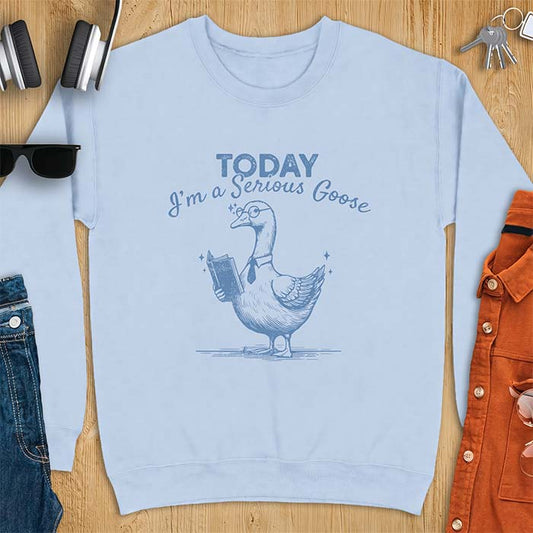 Light Blue sweatshirt with an illustration of a goose wearing round glasses and a necktie, holding an open book, next to sparkle accents and the text Today I'm A Serious Goose.