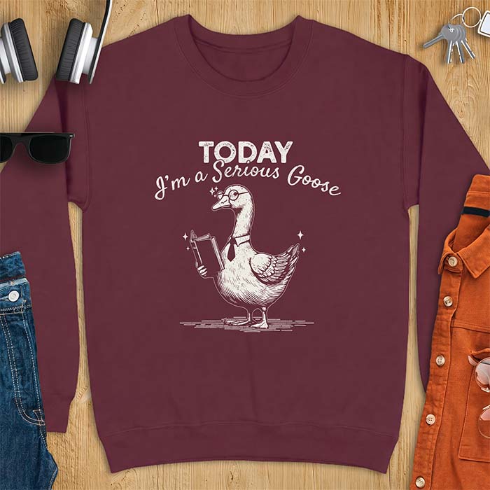 Maroon sweatshirt with an illustration of a goose wearing round glasses and a necktie, holding an open book, next to sparkle accents and the text Today I'm A Serious Goose.