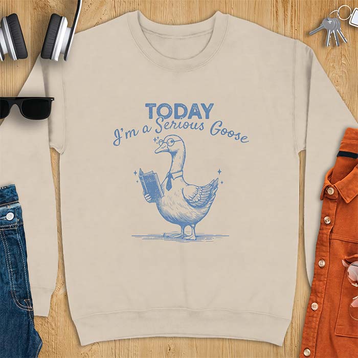 Sand sweatshirt with an illustration of a goose wearing round glasses and a necktie, holding an open book, next to sparkle accents and the text Today I'm A Serious Goose.