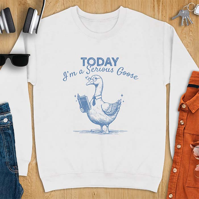 White sweatshirt with an illustration of a goose wearing round glasses and a necktie, holding an open book, next to sparkle accents and the text Today I'm A Serious Goose.