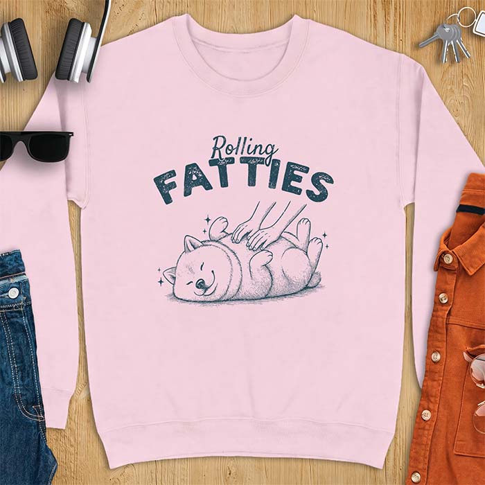 Light Pink sweatshirt with a graphic of a chubby Shiba Inu rolled onto its back getting a belly rub, with sparkles around it and the text Rolling Fatties above.