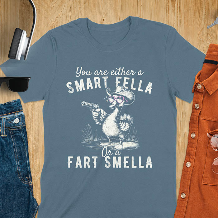 Indigo blue color tee with A goose wearing heart shaped glasses and holding a pistol. Text reads You are either a Smart Fella or a Fart Smella.