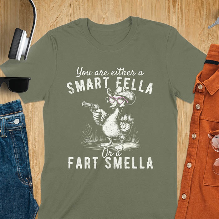 Military green color tee with A goose wearing heart shaped glasses and holding a pistol. Text reads You are either a Smart Fella or a Fart Smella.
