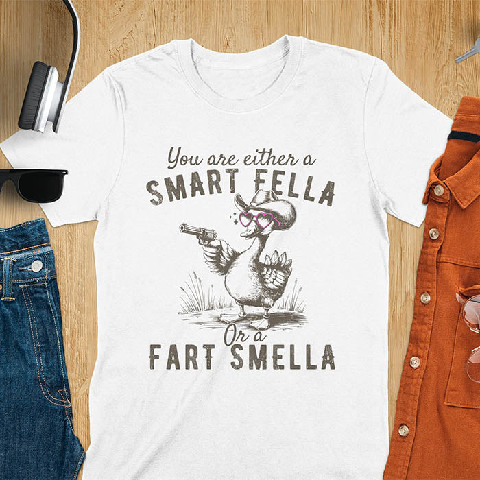 White color tee with A goose wearing heart shaped glasses and holding a pistol. Text reads You are either a Smart Fella or a Fart Smella.