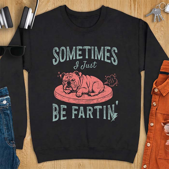 Black sweatshirt with a graphic of a sleeping English Bulldog curled up on a dog bed with a fart cloud drawn behind it beside the text Sometimes I Just Be Fartin