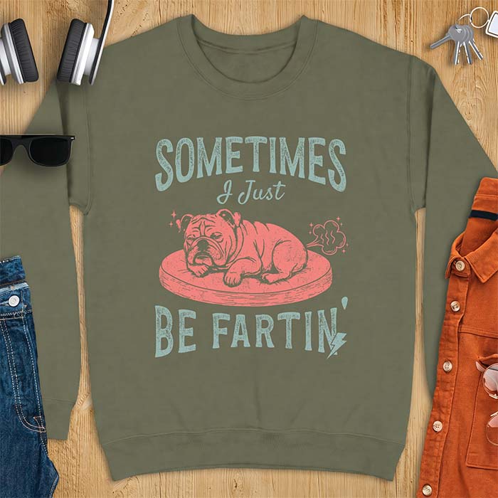 Military Green sweatshirt with a graphic of a sleeping English Bulldog curled up on a dog bed with a fart cloud drawn behind it beside the text Sometimes I Just Be Fartin