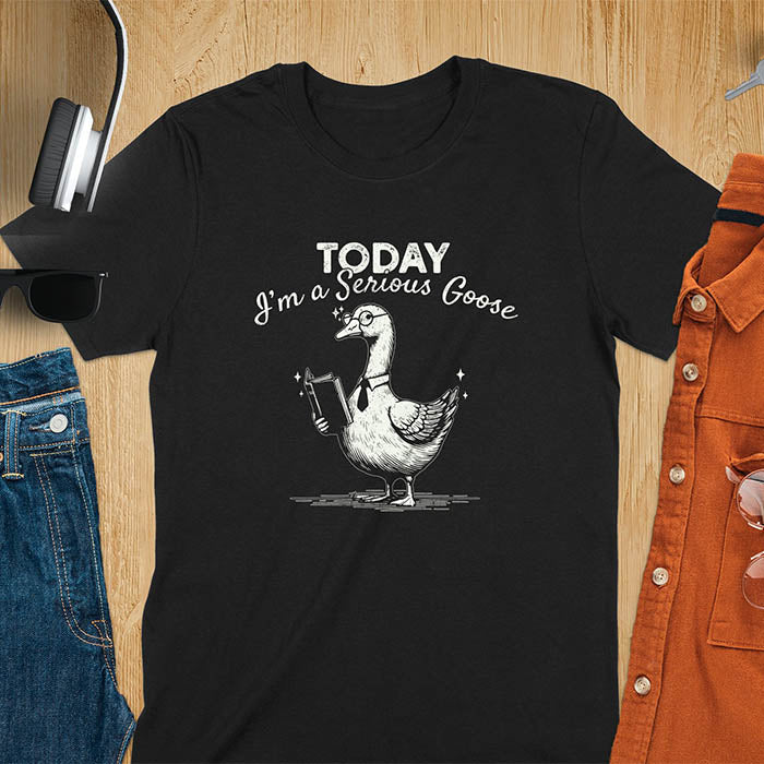 Black color tee Featuring a retro vintage design with a distressed texture effect, this meme graphic tee showcases a dapper goose standing tall with a tie, collar, spectacles, and an open book in its wing, paired with the cheeky text, Today I’m a Serious Goose.