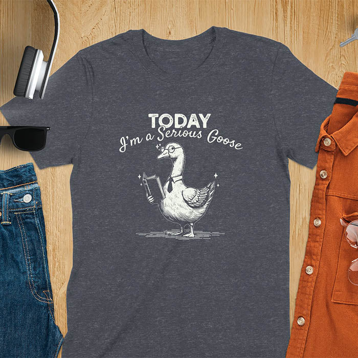 Dark heather color tee Featuring a retro vintage design with a distressed texture effect, this meme graphic tee showcases a dapper goose standing tall with a tie, collar, spectacles, and an open book in its wing, paired with the cheeky text, Today I’m a Serious Goose.