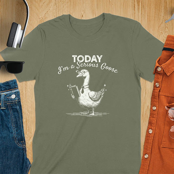 Military green color tee Featuring a retro vintage design with a distressed texture effect, this meme graphic tee showcases a dapper goose standing tall with a tie, collar, spectacles, and an open book in its wing, paired with the cheeky text, Today I’m a Serious Goose.
