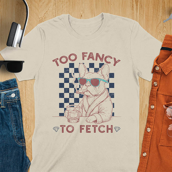 Sand color tee with "Too Fancy To Fetch" text and French Bulldog in sunglasses with whisky and smoking cigar on checkered background