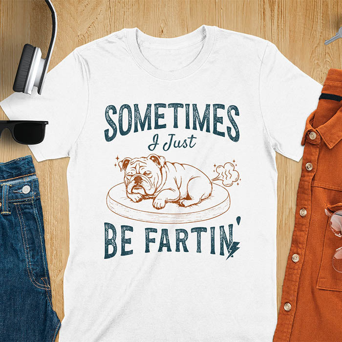 White t-shirt with vintage-inspired bulldog illustration. Retro graphic features snoozing English bulldog on dog bed with text 'Sometimes I Just Be Fartin' in distressed typography. Quirky animal meme design.