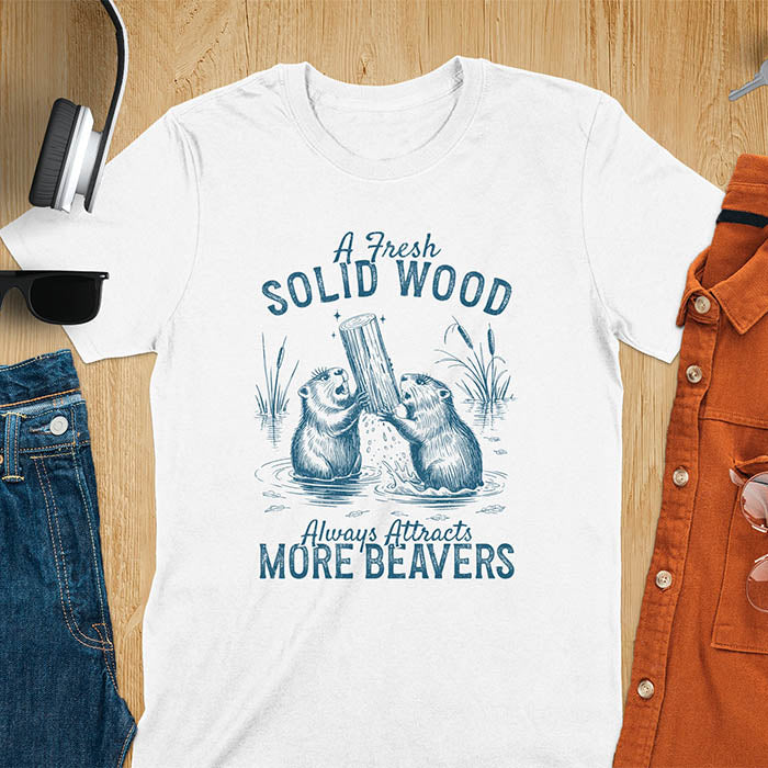 White t-shirt with vintage-style illustration of two beavers in water fighting over a wooden log, featuring text 'A Fresh Solid Wood Always Attracts More Beavers' in rustic lettering 