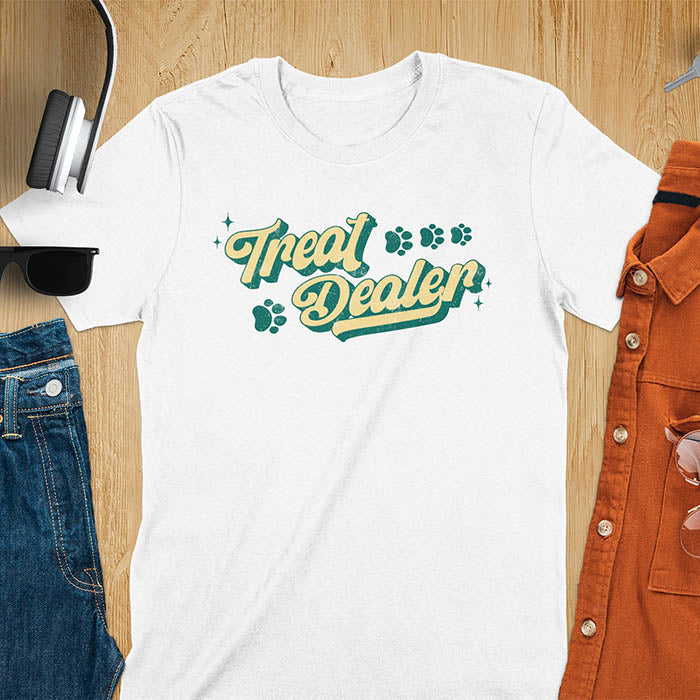 White Light blue t-shirt with Treat Dealer text in retro script typography with green and yellow colors and paw print decorations